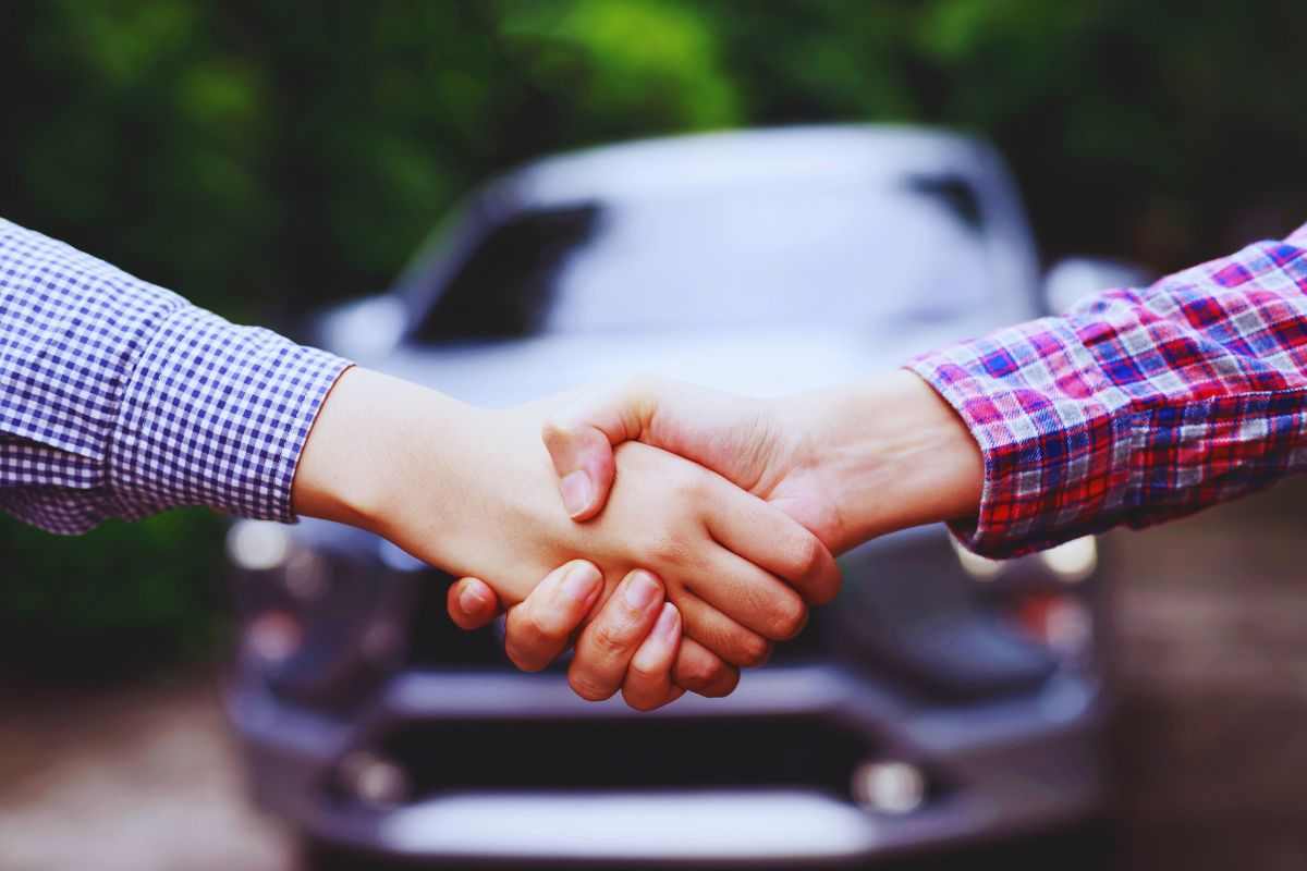 Persone che si stringono la mano davanti ad un'auto