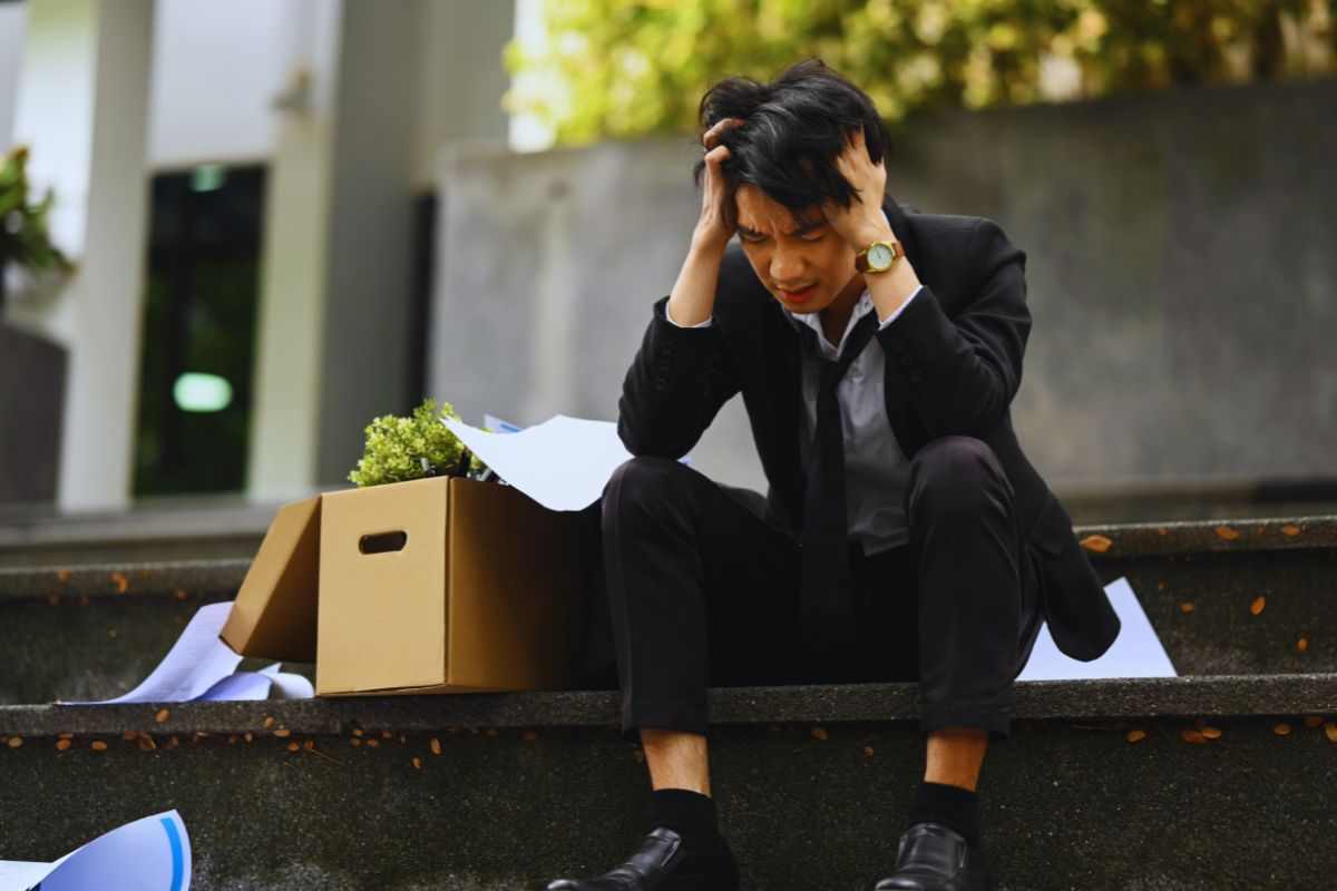 Lavoratore licenziato seduto sulle scale dell'azienda con i suoi effetti personali accanto