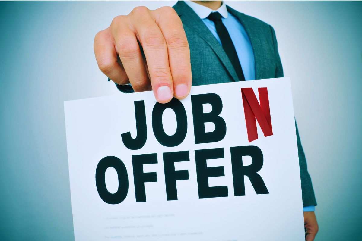 Uomo che mostra un foglio con su scritto "Job Offer" e logo Netflix