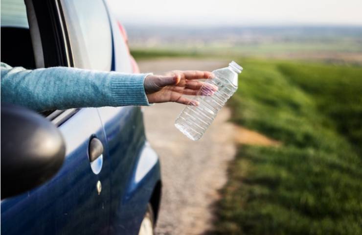 donna che getta bottiglia di plastica dall'auto