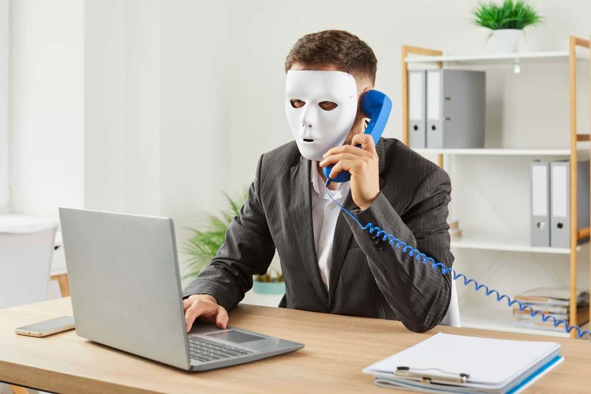 Uomo con maschera al telefono davanti PC