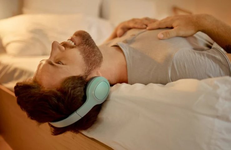 Uomo sdraiato sul letto ascolta la musica con le cuffie 