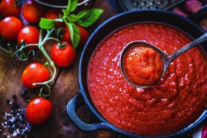 Pentola piena di salsa accanto a pomodori maturi