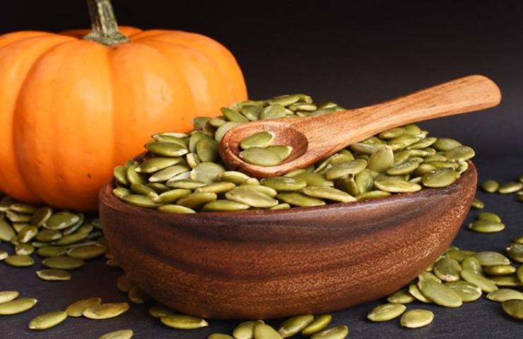 Ciotola colma di semi di zucca con una zucca sullo sfondo
