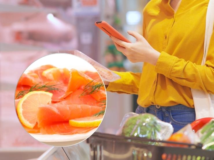 donna che fa la spesa al supermercato e guarda il cellulare