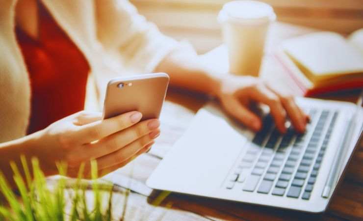 persona al computer con smartphone in mano