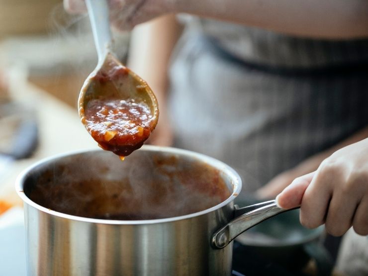 cuocere sugo, primo piano su cucchiaio di legno che mostra il sugo nella pentola