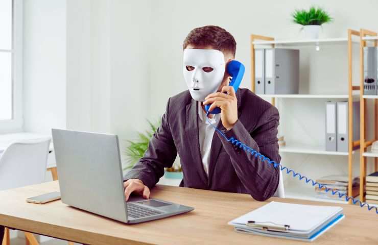uomo al computer e al telefono con una maschera bianca
