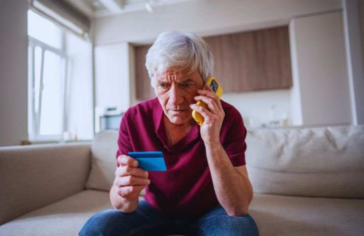 anziano al telefono e con una carta in mano