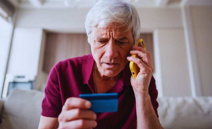 anziano al telefono con carta in mano